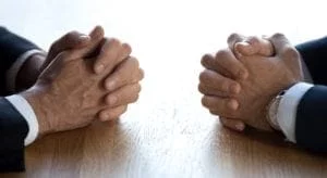 #alt_tagClasped hands of two businessmen negotiators opponents opposite on table